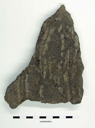 Fragment of lavastone quern with roughly tooled grinding surface, other side is worn, possibly turned over for reuse