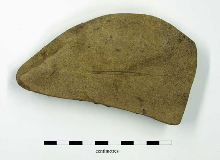Fragment of irregular whetstone with areas of worn edge and sharpening grooves on upper and lower faces. 129 x 73 x 22.5mm