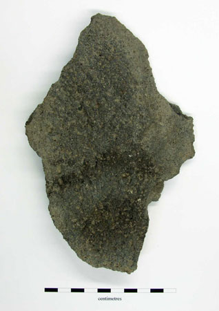 Fragment of lavastone quern with rough tooling and sooting, no diagnostic features present. 22mm thick